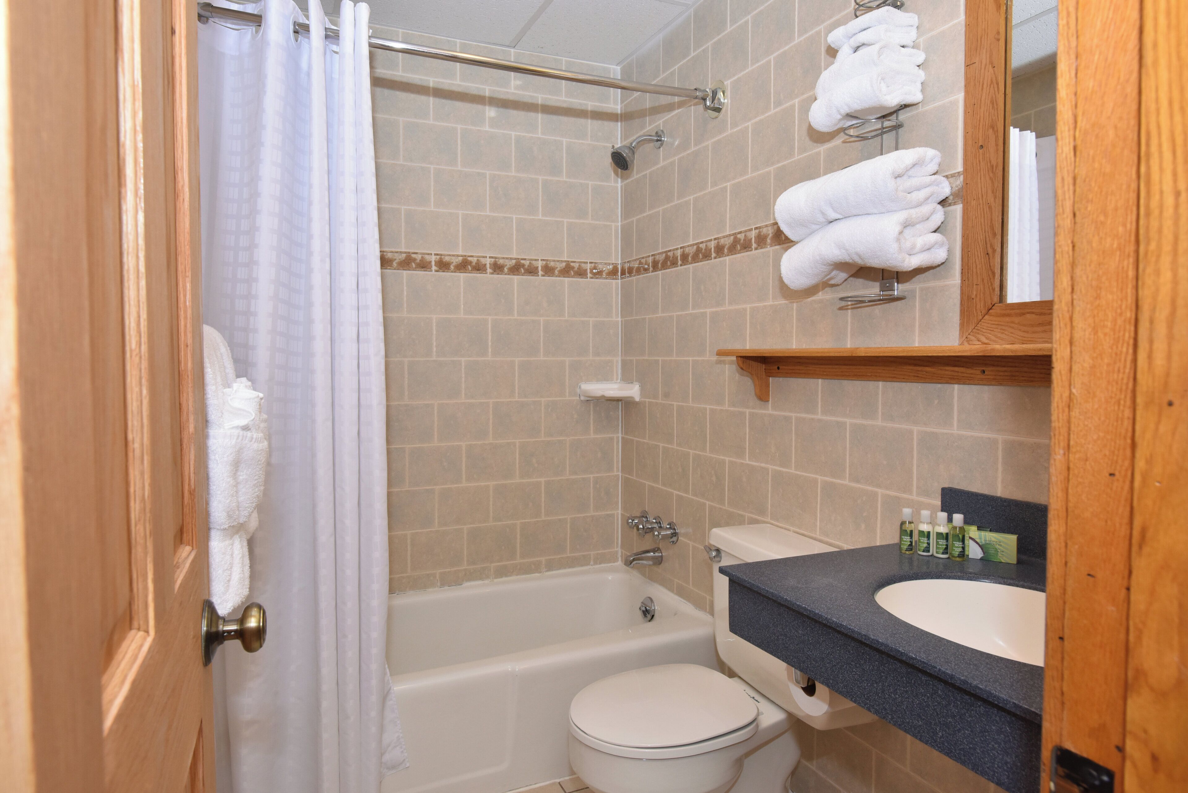 A bathroom with a bathtub, toilet, and sink. There are towels hanging on a rack and toiletries on the sink.