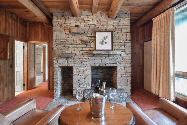 A stone fireplace with a framed botanical print above it, flanked by wooden walls and a red carpeted floor.