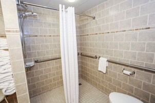 Un baño con azulejos color crema, un inodoro blanco, una ducha con cortina blanca y barras de apoyo.