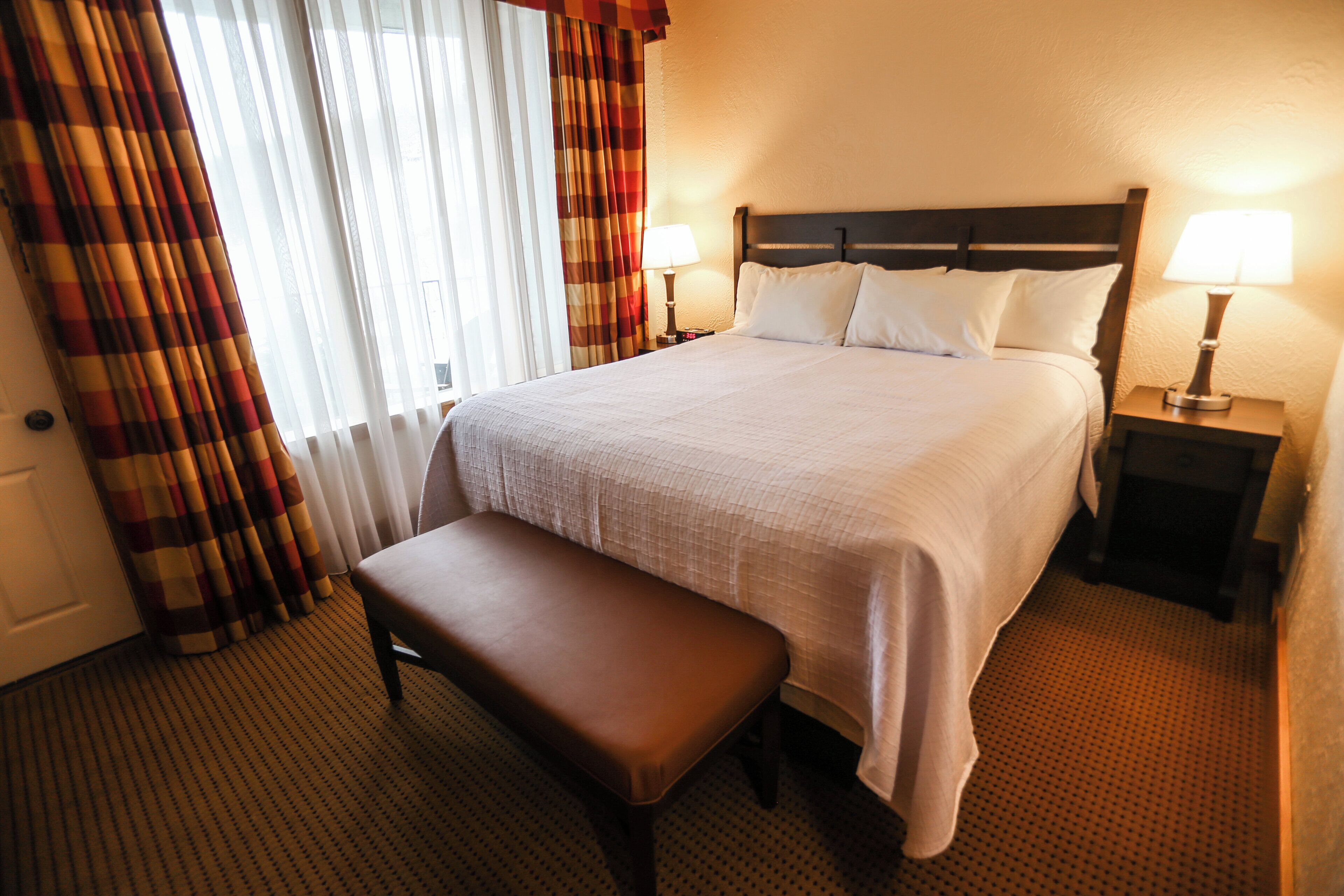 Una camera d'albergo con un letto grande, due lampade ai lati del letto, una panca e una finestra con tende.