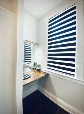 Bathroom features a single vanity with a mirror above and a window with horizontal blinds.