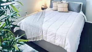 A bedroom with a bed, bedside table, lamp, and a potted plant. - Newly Renovated 3 Bed, 2 Bath Apartm! 24/7 Service (Covington)