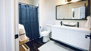 A modern bathroom with a shower, toilet, and a vanity with a large mirror. - Newly Renovated 3 Bed, 2 Bath Apartm! 24/7 Service (Covington)