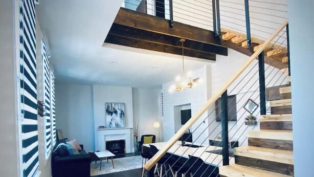 A modern living room with a fireplace, a staircase with wooden steps and metal railings, and a black leather sofa. - Newly Renovated 3 Bed, 2 Bath Apartm! 24/7 Service (Covington)