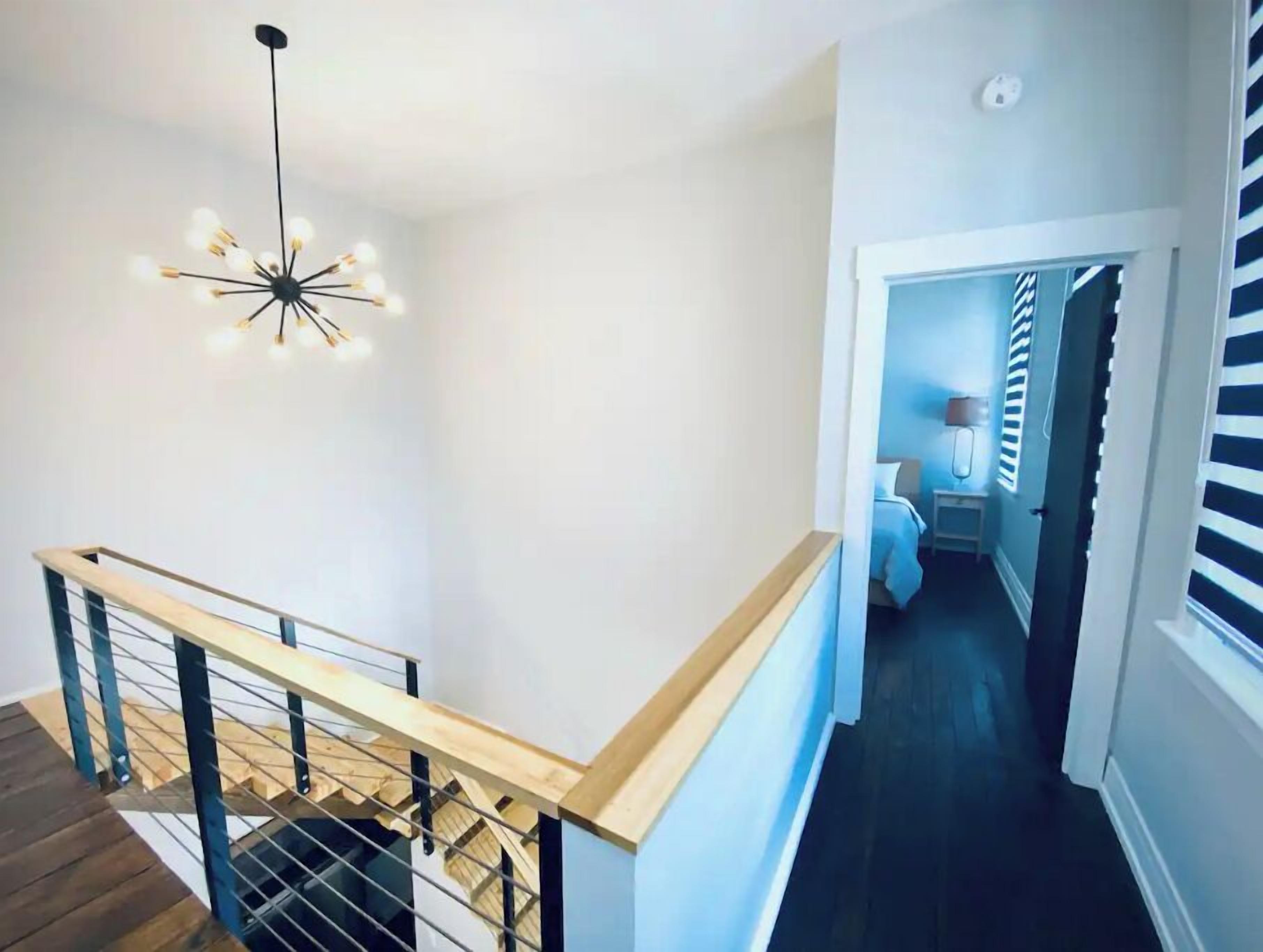 Un escalier doté d’une rampe en bois et de balustrades en métal, menant à une chambre à coucher avec un lit et une table de chevet.