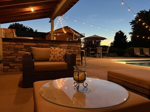 Relax on the patio with comfortable seating and a glass table, surrounded by a pool and covered seating area.