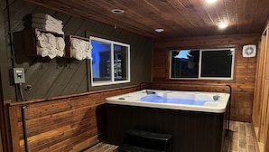 Un interior de madera con una bañera de hidromasaje, paredes de madera, un ventanal y un perchero.