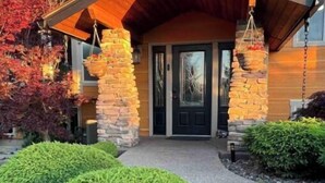 Una casa moderna con fachada de piedra, techo de madera y un jardín delantero cuidado con setos podados.