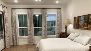 A bedroom with a large bed, a nightstand with a lamp, a painting on the wall, and a window with curtains. - Spacious 4 Bedroom House - 3/4 Mile to Round Top Center! (Round Top)