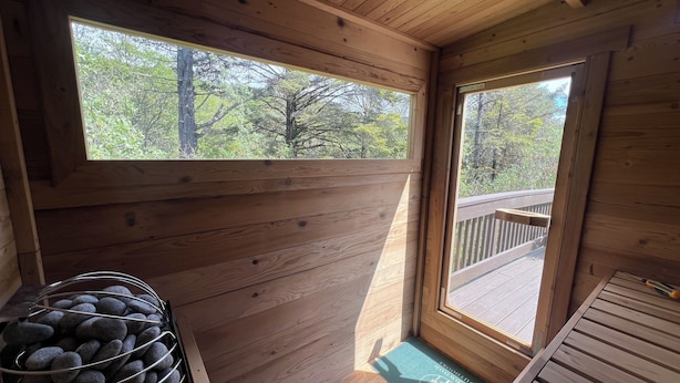 Innenansicht einer Holzhütte mit einer Holzdielen-Terrasse, einem Metallkorb voller Steine und einer Fußmatte.