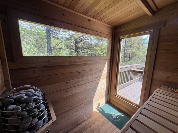 A wooden cabin interior with a wooden deck outside, a metal basket of rocks, and a doormat.