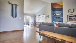 Ein modernes Wohnzimmer mit einer Holzbank, einem grauen Sofa und einem Essbereich mit Stühlen und einem Tisch.