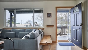 Ein modernes Wohnzimmer mit einem großen Fenster, einer hölzernen Bank und einer dunklen Tür, die nach draußen führt.