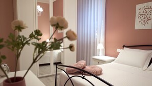 Een slaapkamer met een bed, nachtkastje, spiegel en een vaas met bloemen.