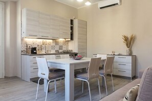 A modern kitchen with white cabinetry, a dining table with chairs, and a small island with a coffee machine. - Just 350 meters from the historic center! Recently Renovated Art Nouveau House (Noto)