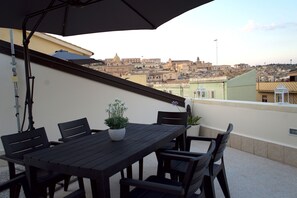 Una terraza con una mesa, sillas, una planta en maceta y vistas a un paisaje urbano.