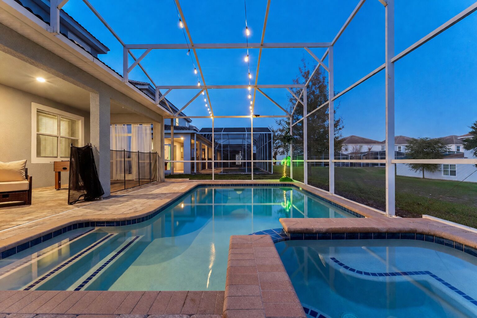 A swimming pool with a covered area, a sofa, and a chair, surrounded by a fence.