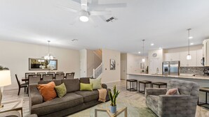 Una sala moderna con sofá, sillón y mesa de centro. Se ve, al fondo, un área de comedor con sillas y una mesa.