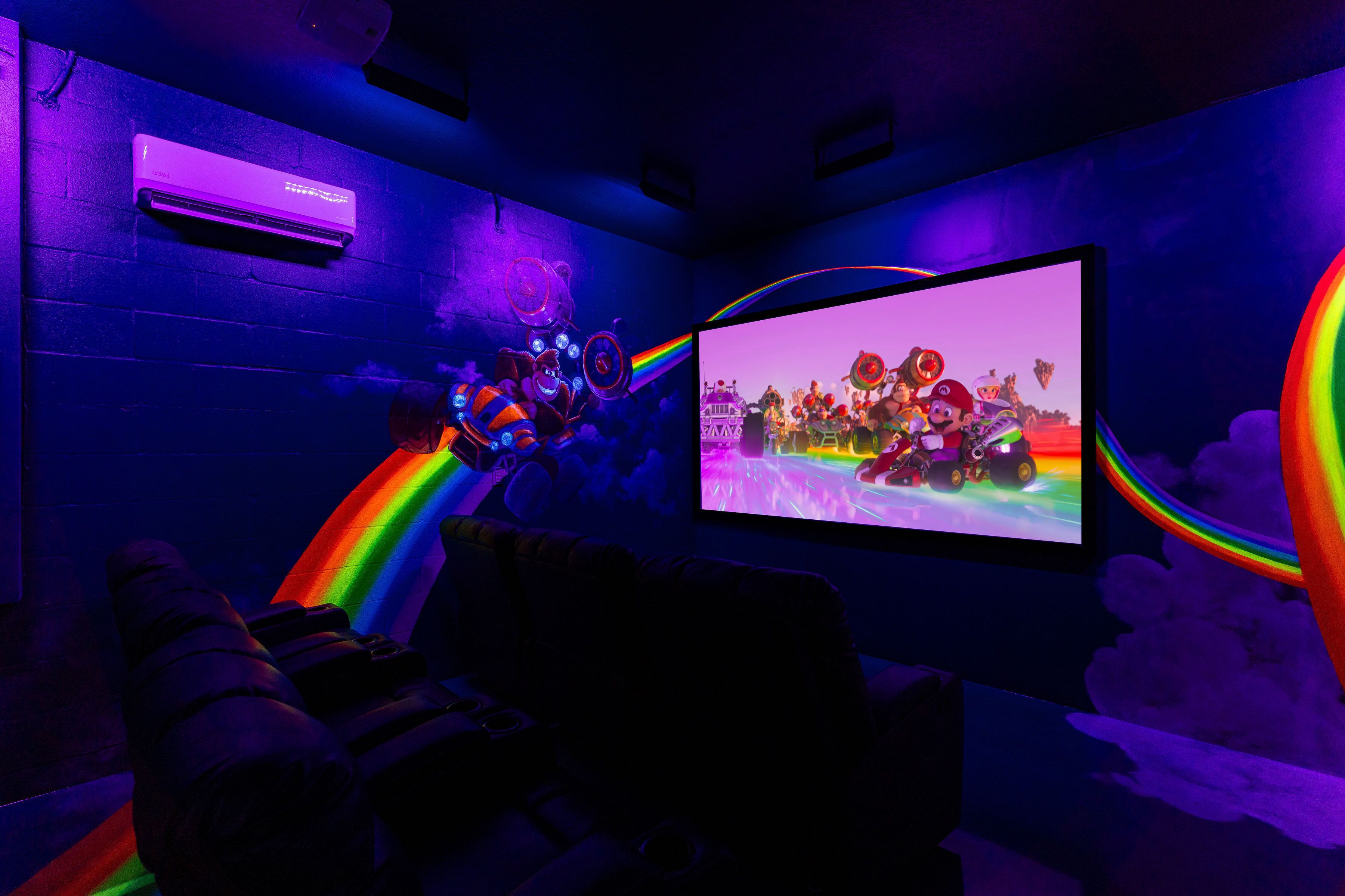 A room with a large screen displaying a video game, a wall-mounted air conditioner, and a ceiling with a light fixture.