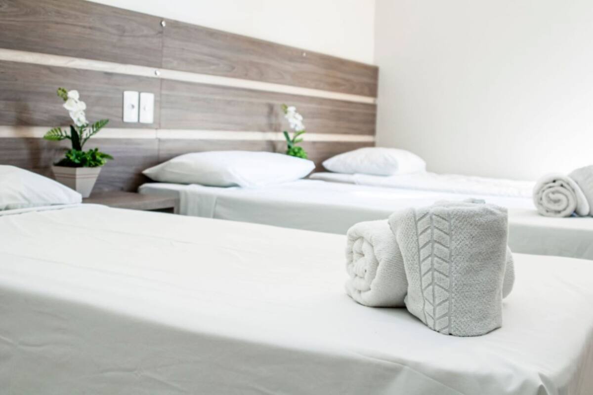 A hotel room with two beds, white linens, a wooden headboard, and a potted plant.