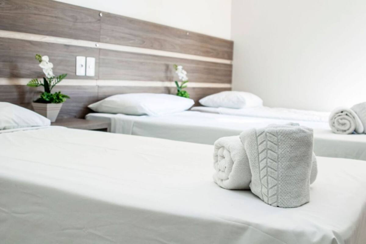 A hotel room with two beds, white linens, a wooden headboard, and a potted plant.