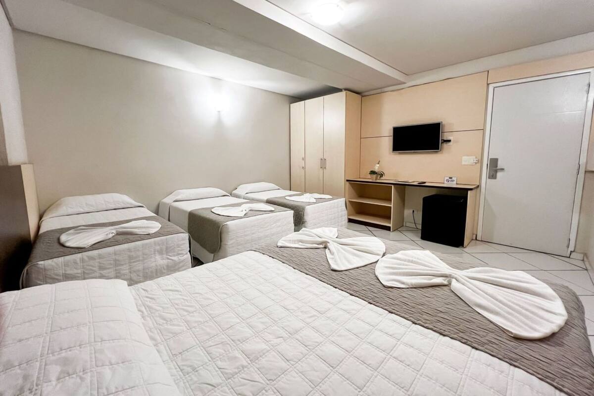 A hotel room with four beds, a desk, a television, and a wardrobe.