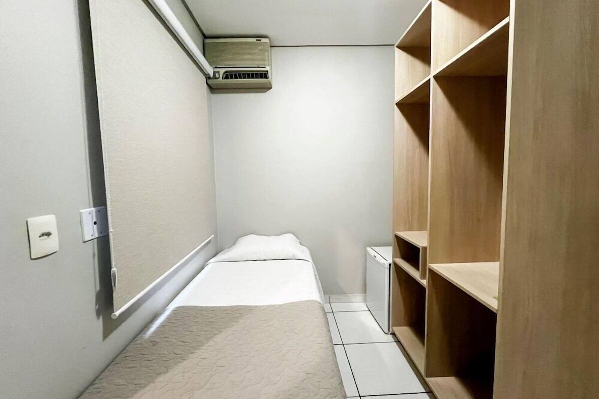 A small, narrow room with a bed, a wooden wardrobe, a white radiator, and a white toilet.