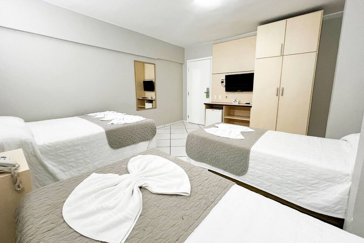 A hotel room with two beds, a TV, a wardrobe, and a small desk with a telephone.
