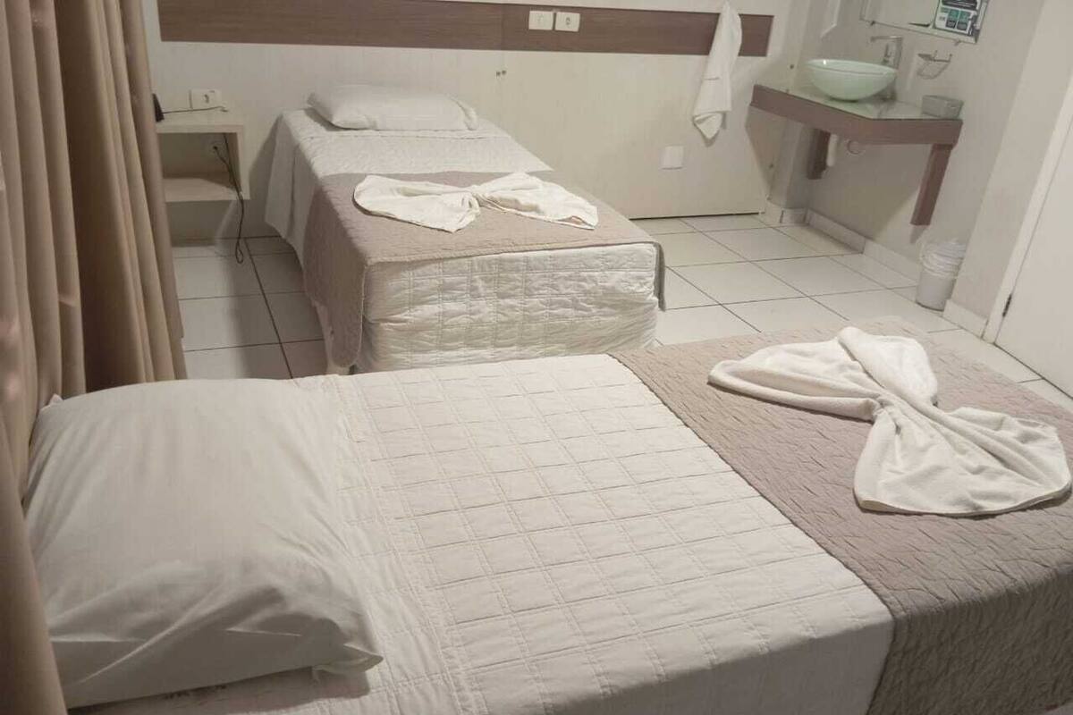 A hotel room with two beds, a bathroom with a sink, and a mirror.