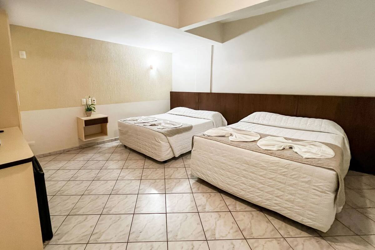 A hotel room with two beds, a small bedside table, and a nightstand.