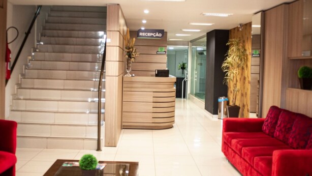 Un área de recepción con una escalera, un mostrador de recepción, un sofá rojo y una mesa de centro.