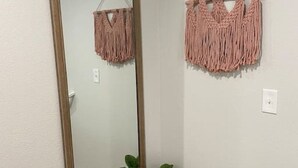A mirror with a wooden frame, a macrame wall hanging, and a potted plant in a corner.