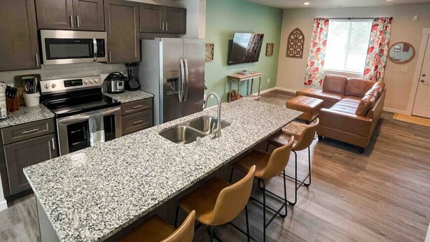 A modern kitchen with granite countertops, stainless steel appliances, and a bar area with stools.