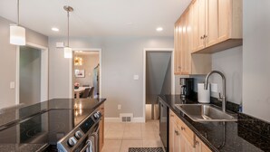A modern kitchen with a black countertop, stainless steel appliances, wooden cabinets, and a pendant light. - BEST LOCATION DOWNTOWN, DESIGNER FURNISHINGS (Salt Lake City)