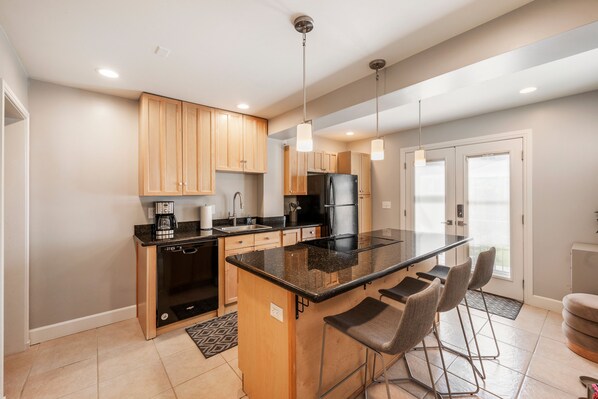 A modern kitchen with wooden cabinets, a black countertop, and a built-in island with bar stools. - BEST LOCATION DOWNTOWN, DESIGNER FURNISHINGS (Salt Lake City)