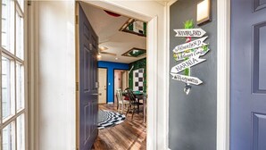 Un couloir avec un tapis à carreaux noirs et blancs, un mur orné d’indications vers des lieux imaginaires, et un mur bleu à motifs à carreaux.
