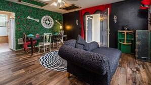 Une pièce comprenant un lit, une table à manger avec des chaises, une horloge au mur et un ventilateur de plafond.