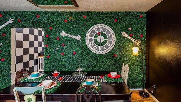 Un coin repas avec une table à carreaux, une horloge et un mur vert orné de roses rouges.