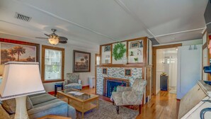 A living room with a fireplace, a ceiling fan, and a large window. - Cozy Mount Dora Cottage /Walk Downtown/ Pet Friendly / Fenced Yard (Mount Dora)