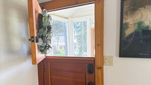 A wooden front door with a small window above it, a doormat, and a framed artwork on the wall. - Cozy Mount Dora Cottage /Walk Downtown/ Pet Friendly / Fenced Yard (Mount Dora)