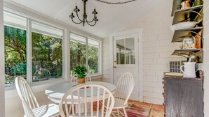 A bright kitchen with white cabinetry, a round dining table, and chairs. There is a chandelier hanging from the ceiling, and a window with a view of greenery outside. - Cozy Mount Dora Cottage /Walk Downtown/ Pet Friendly / Fenced Yard (Mount Dora)
