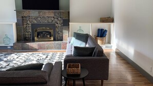 Una sala de estar con chimenea, un sofá, una mesa de centro y un televisor montado en la pared.