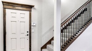 A hallway with a white door, a thermostat, and a wooden staircase with carpeted steps.