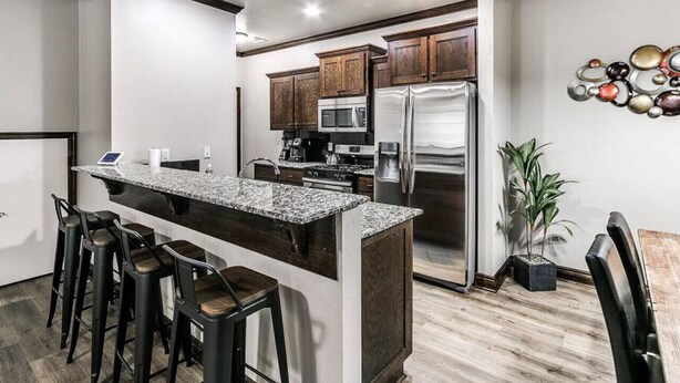 A modern kitchen with a central island, bar stools, wooden cabinets, stainless steel appliances, and a decorative wall piece.