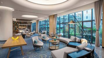 A spacious lobby with a curved sofa, round tables, and a wooden coffee table. Large windows offer a view of the outdoors.