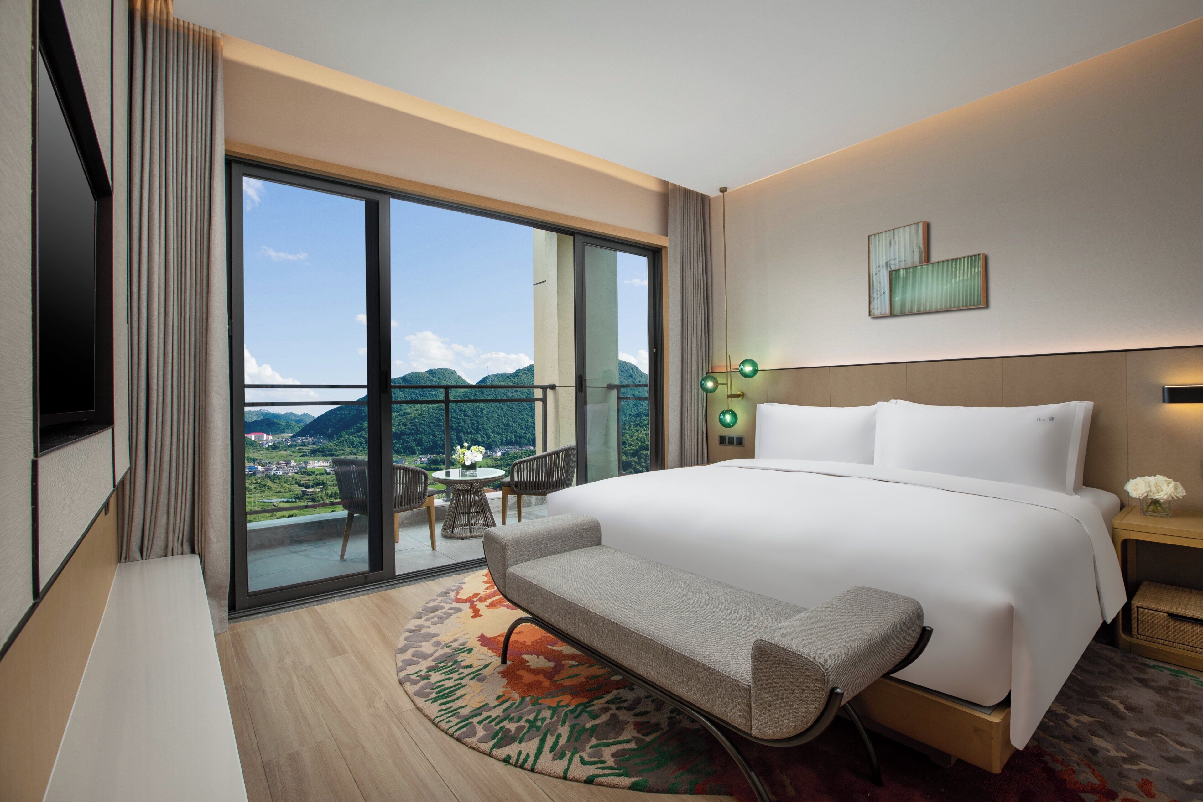 Ein Hotelzimmer mit einem großen Bett, einer Bank, einem kleinen Tisch mit Stühlen und Bergblick durch ein großes Fenster.