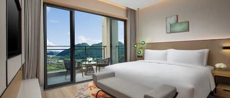 Ein Hotelzimmer mit einem großen Bett, einer Bank, einem kleinen Tisch mit Stühlen und Bergblick durch ein großes Fenster.