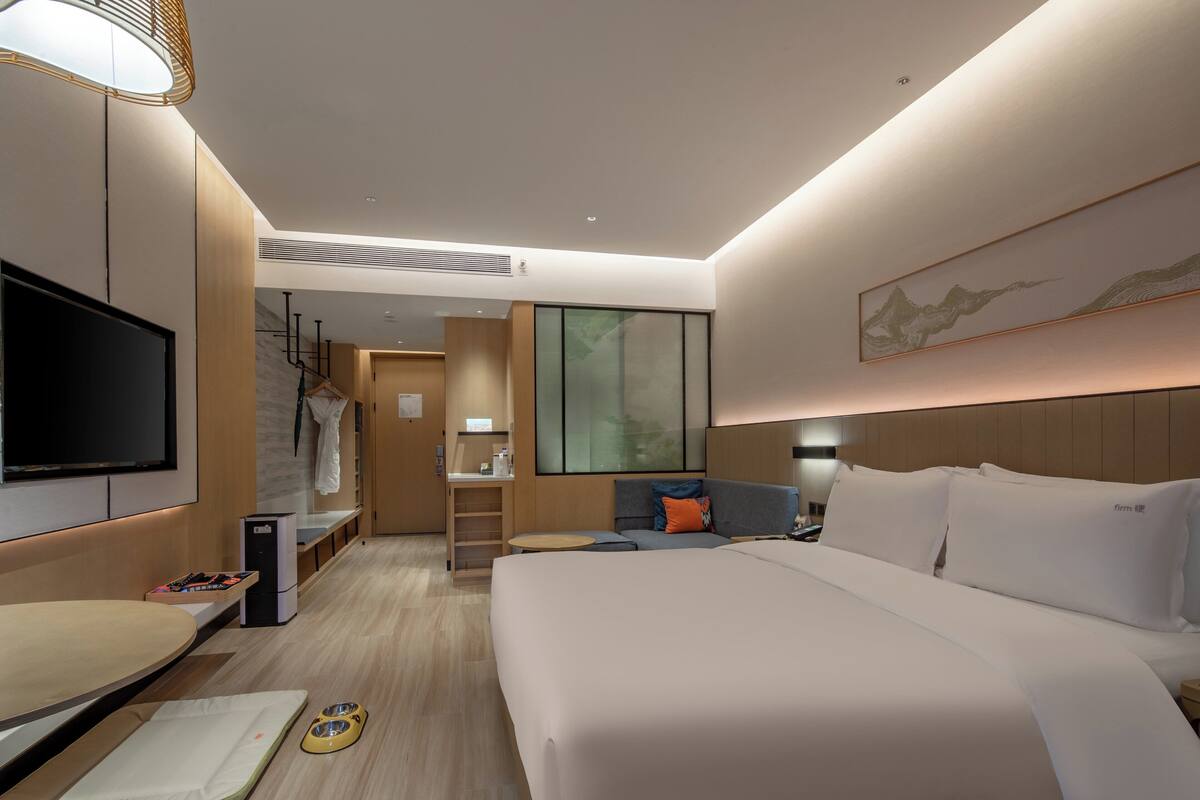 A modern hotel room with a large bed, a flat-screen TV, a desk, and a seating area.