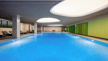 A large indoor swimming pool with a blue floor, surrounded by lounge chairs and a green wall.