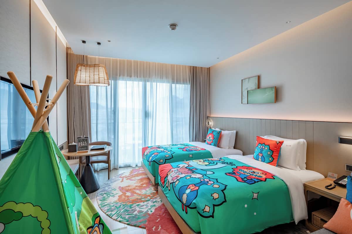 A hotel room with a bed, a desk, a chair, a window with curtains, and a view of the outdoors.